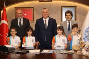 BAŞKAN GÜREL KOLTUĞUNU 4 İLKOKUL ÖĞRENCİSİNE TESLİM ETTİ